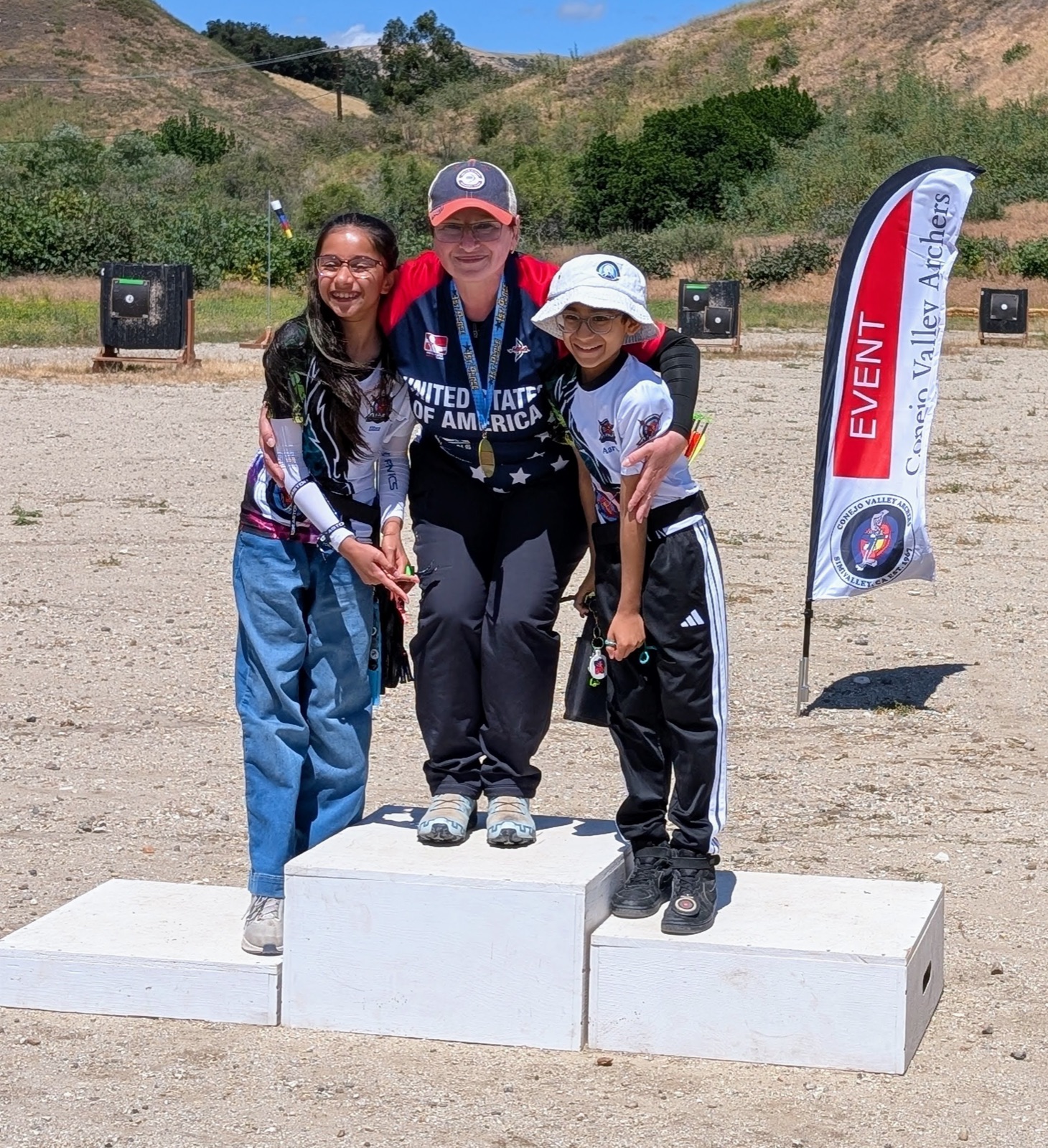 Coach Marianna and two students celebrating on the podium at a Conejo Valley Archers event