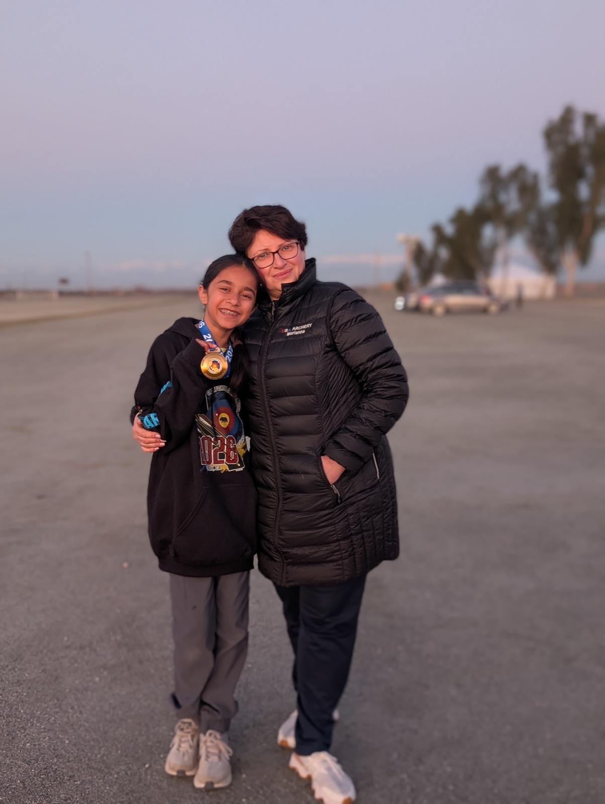 Coach Marianna with a young archery student holding her gold medal
